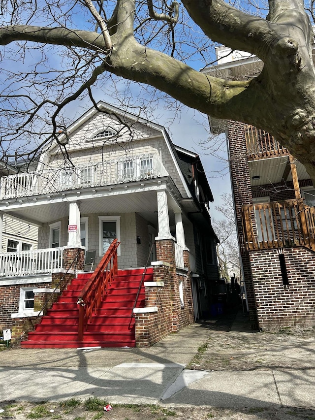 view of front facade with a balcony, covered porch, and a gambrel roof