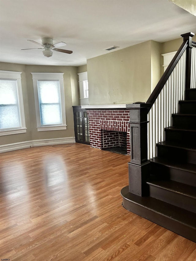 living room featuring stairway, baseboards, light wood-style flooring, a fireplace, and ceiling fan