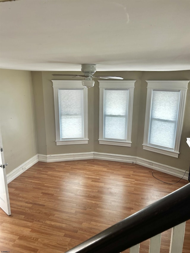 empty room featuring wood finished floors, baseboards, and ceiling fan