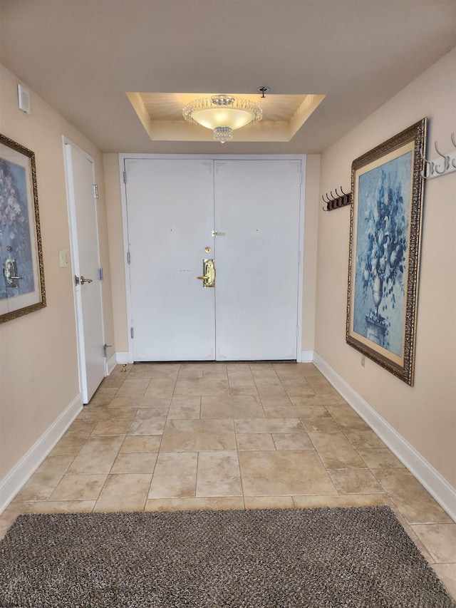 interior space featuring light tile patterned floors, a tray ceiling, and baseboards