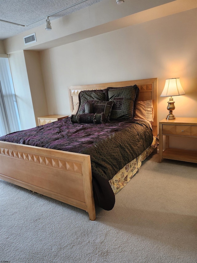 carpeted bedroom with track lighting, visible vents, and a textured ceiling