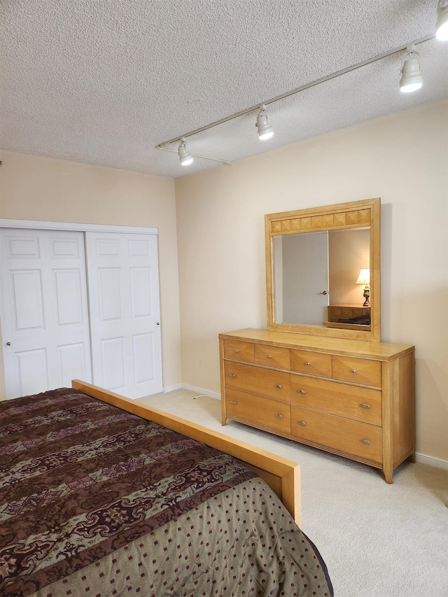 bedroom featuring track lighting, a textured ceiling, a closet, baseboards, and light colored carpet