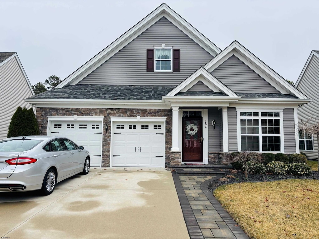 view of front of home featuring a garage, stone siding, roof with shingles, and driveway