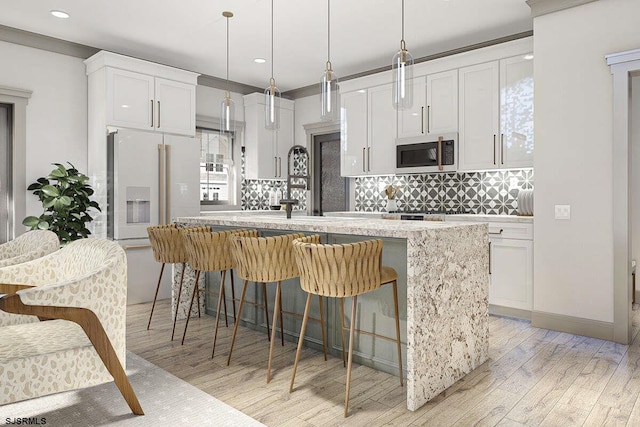 kitchen with light wood-style flooring, an island with sink, white cabinetry, stainless steel microwave, and backsplash