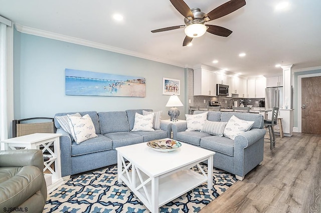 living room featuring ornamental molding, a ceiling fan, recessed lighting, light wood finished floors, and decorative columns