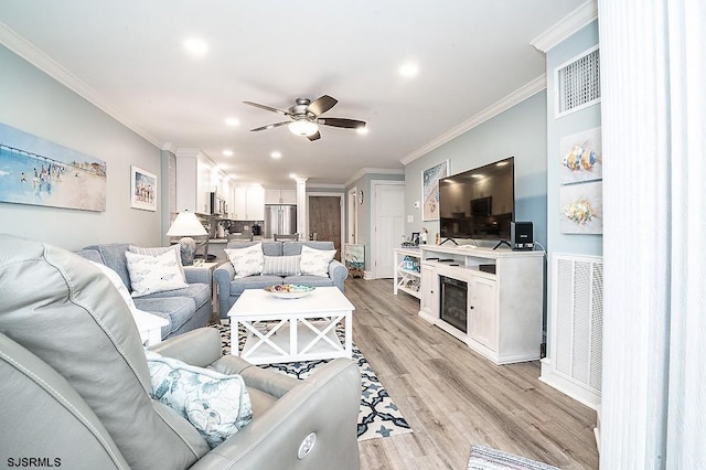 living room featuring light wood-style floors, visible vents, a ceiling fan, and crown molding