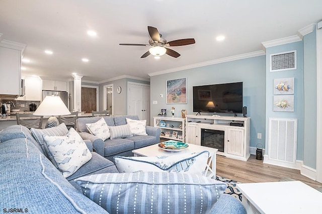 living room featuring visible vents, light wood-type flooring, crown molding, and ceiling fan