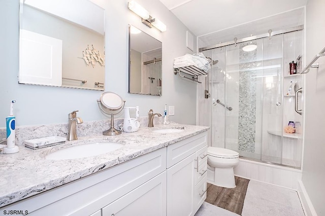 full bath with double vanity, a stall shower, wood finished floors, and a sink