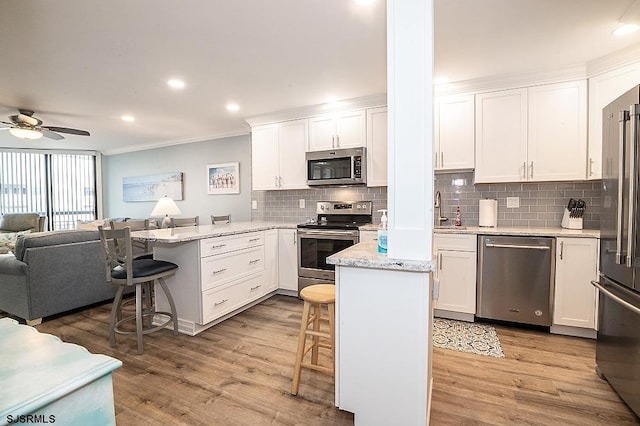 kitchen with open floor plan, appliances with stainless steel finishes, a peninsula, a kitchen breakfast bar, and white cabinetry