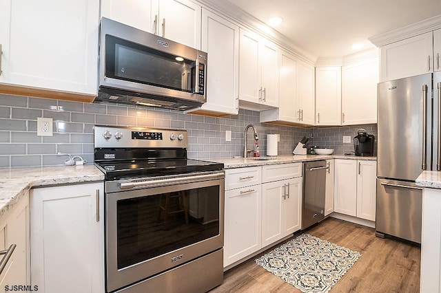 kitchen with a sink, white cabinetry, appliances with stainless steel finishes, light wood finished floors, and decorative backsplash