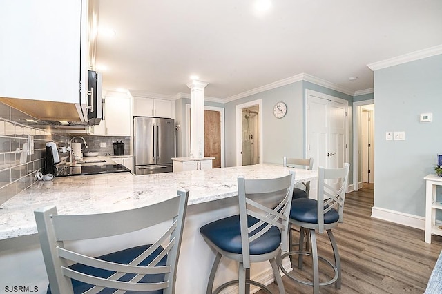 kitchen with tasteful backsplash, wood finished floors, high quality fridge, a peninsula, and ornate columns