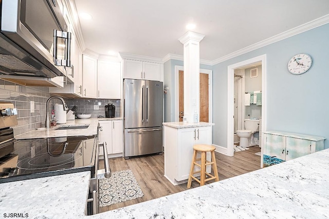 kitchen featuring appliances with stainless steel finishes, light wood-type flooring, ornate columns, and crown molding