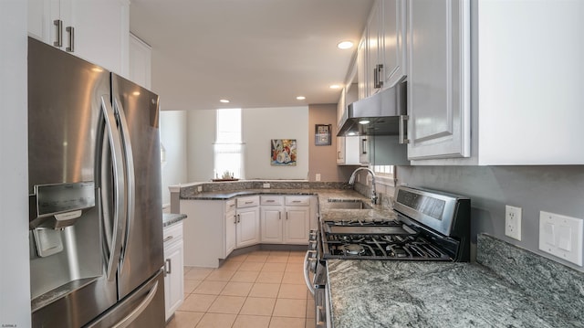 kitchen featuring light tile patterned floors, dark stone countertops, range hood, stainless steel appliances, and a sink