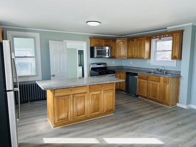 kitchen featuring radiator, a kitchen island, a sink, light wood-style floors, and appliances with stainless steel finishes