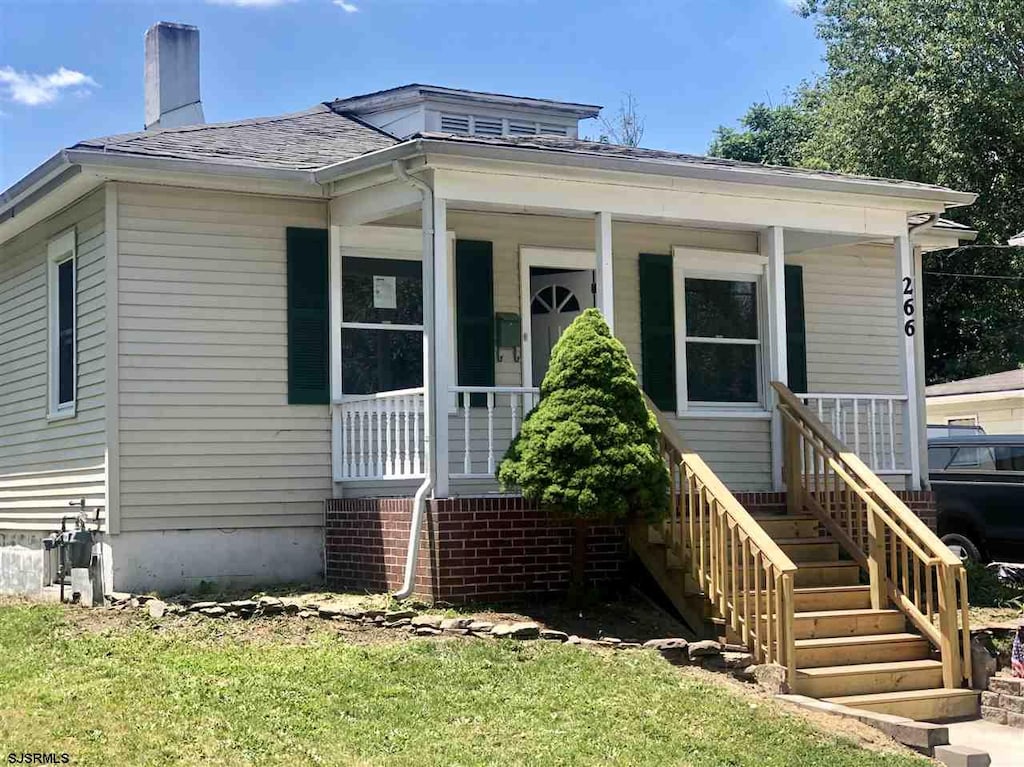 bungalow featuring stairway, a chimney, covered porch, and a shingled roof