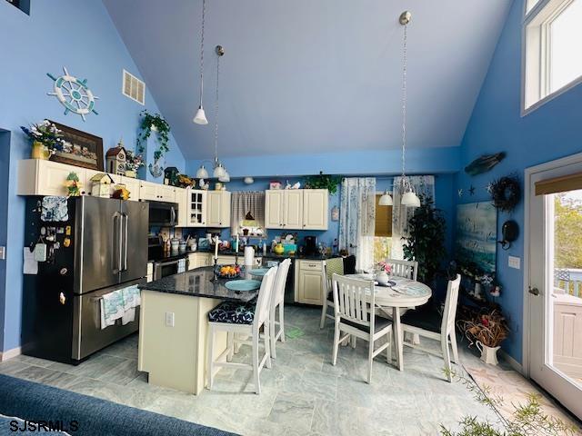 kitchen featuring dark countertops, visible vents, a kitchen island, high vaulted ceiling, and stainless steel appliances