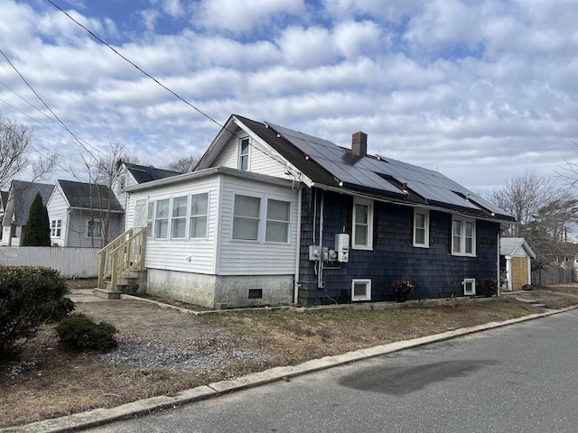 view of front of house with crawl space, roof mounted solar panels, a chimney, and fence