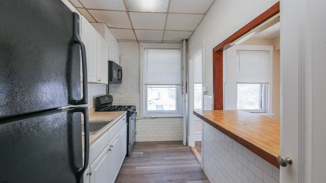 kitchen featuring black appliances, a drop ceiling, wood counters, wood finished floors, and white cabinetry