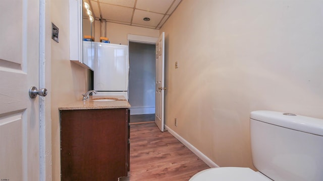 half bathroom featuring baseboards, toilet, wood finished floors, vanity, and a paneled ceiling