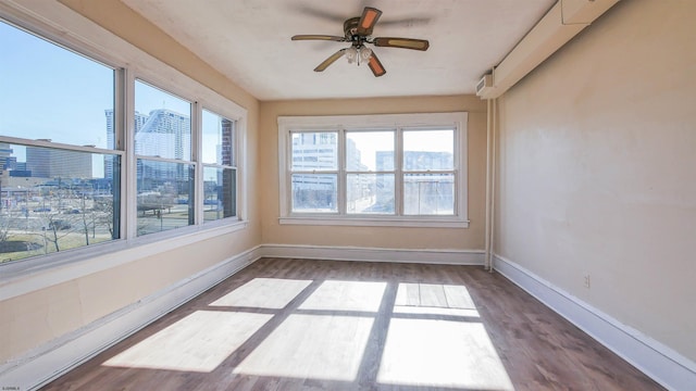 unfurnished sunroom with a city view, a ceiling fan, and a baseboard radiator