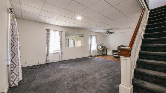 unfurnished living room with stairway, radiator, carpet, baseboards, and ceiling fan