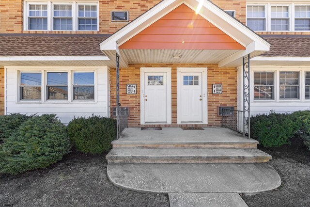 doorway to property with brick siding and roof with shingles