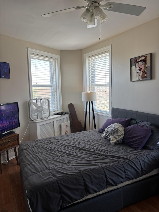 bedroom featuring multiple windows, wood finished floors, ceiling fan, and radiator heating unit