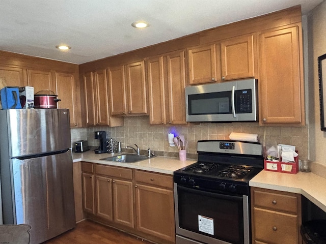 kitchen featuring light countertops, tasteful backsplash, stainless steel appliances, a sink, and brown cabinets