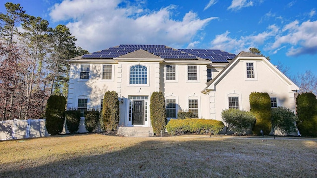 view of front of house with stucco siding, fence, roof mounted solar panels, and a front yard