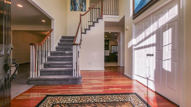 foyer entrance featuring stairway, recessed lighting, baseboards, a towering ceiling, and wood finished floors