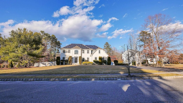french provincial home featuring solar panels, fence, a front lawn, and stucco siding
