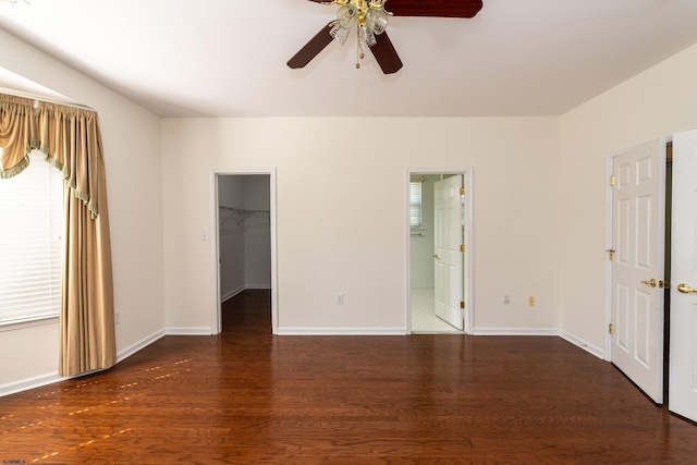 unfurnished bedroom with a spacious closet, ceiling fan, wood finished floors, and baseboards