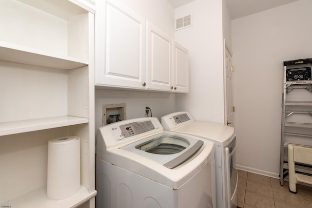 clothes washing area featuring washing machine and dryer, visible vents, light tile patterned flooring, and cabinet space