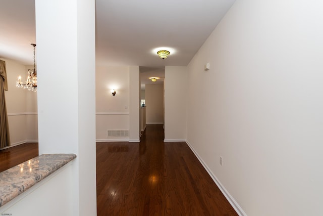 hall with visible vents, baseboards, an inviting chandelier, and dark wood finished floors
