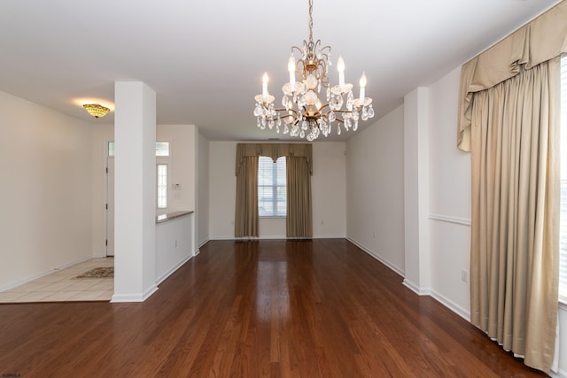 empty room featuring baseboards, an inviting chandelier, and wood finished floors