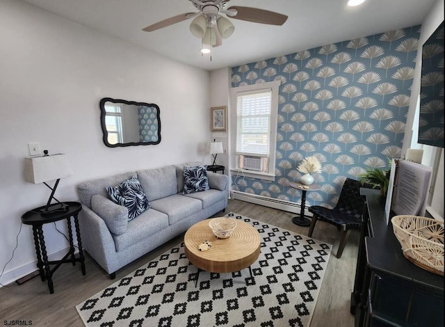 living area featuring ceiling fan, a baseboard heating unit, baseboards, and wood finished floors