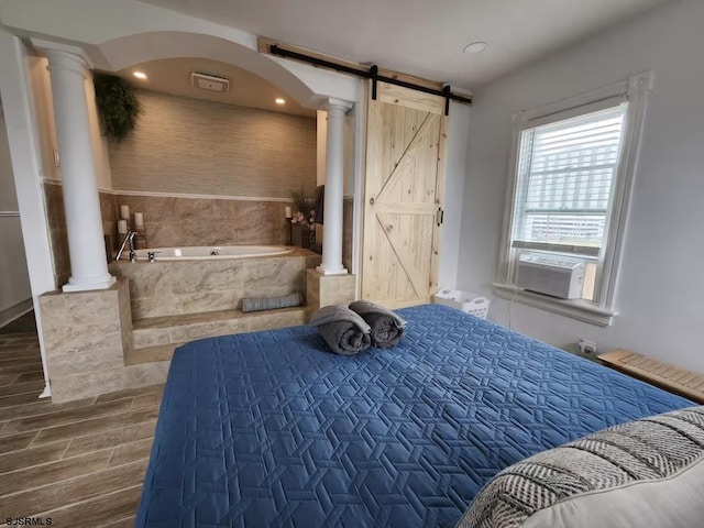 bedroom featuring cooling unit, a barn door, decorative columns, arched walkways, and wood finished floors