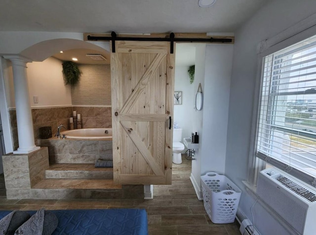 bathroom featuring a bath, toilet, wood tiled floor, ornate columns, and a baseboard heating unit
