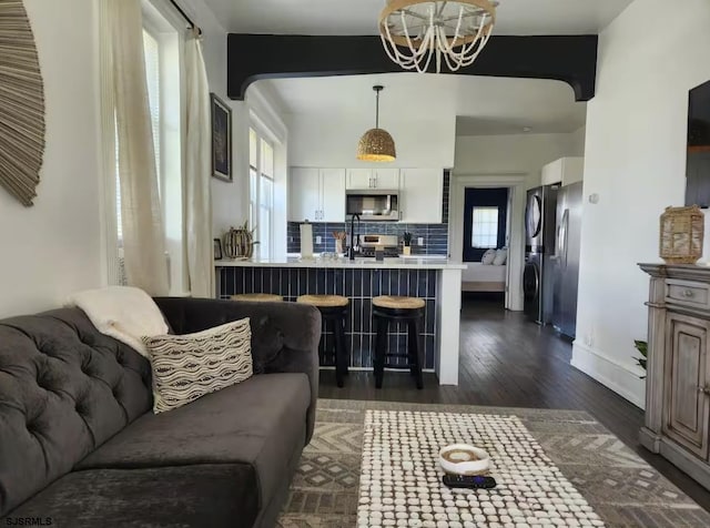 living area featuring plenty of natural light, an inviting chandelier, beam ceiling, and dark wood finished floors