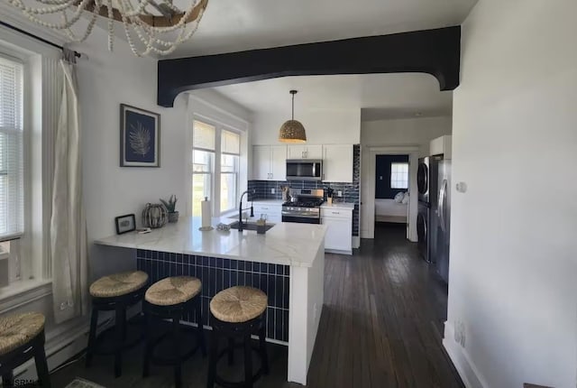 kitchen featuring white cabinets, a sink, appliances with stainless steel finishes, a kitchen breakfast bar, and a peninsula