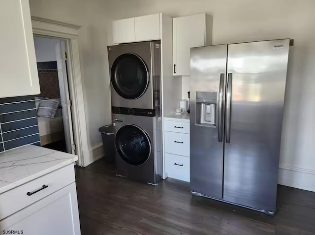 laundry area featuring dark wood-style flooring, baseboards, stacked washing maching and dryer, and laundry area