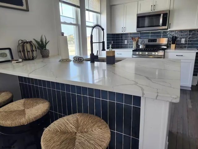 kitchen featuring stainless steel appliances, a peninsula, white cabinets, and backsplash