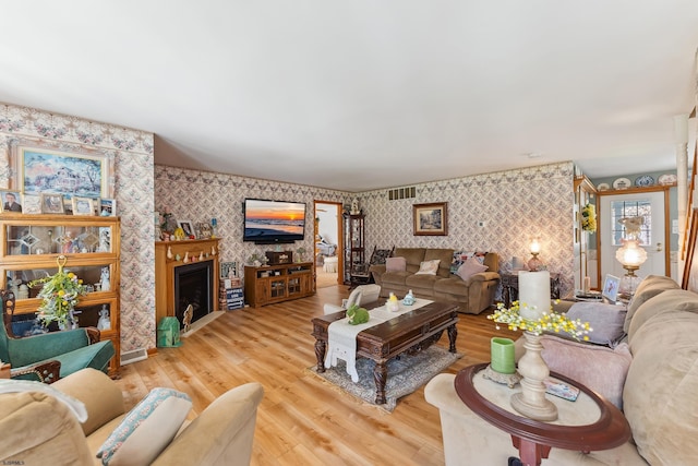 living room with wallpapered walls, light wood-style flooring, and visible vents