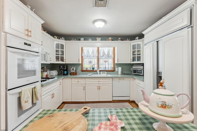 kitchen with glass insert cabinets, light countertops, white appliances, and a sink