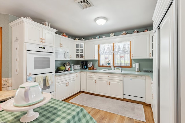kitchen with a sink, visible vents, glass insert cabinets, white appliances, and light countertops