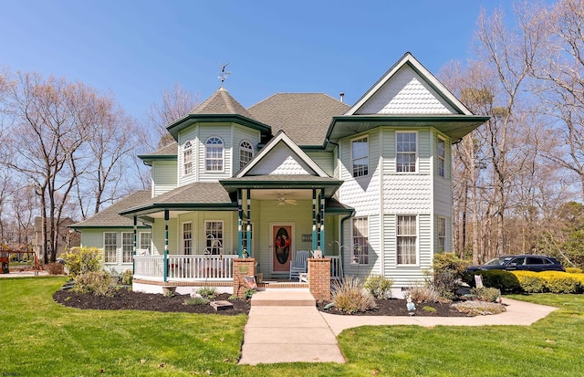 victorian-style house with a porch, a shingled roof, ceiling fan, and a front yard