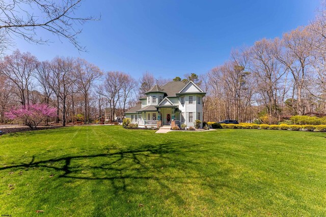 back of property with covered porch, a yard, and roof with shingles