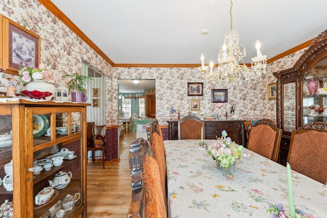 dining room with an inviting chandelier, ornamental molding, and wallpapered walls