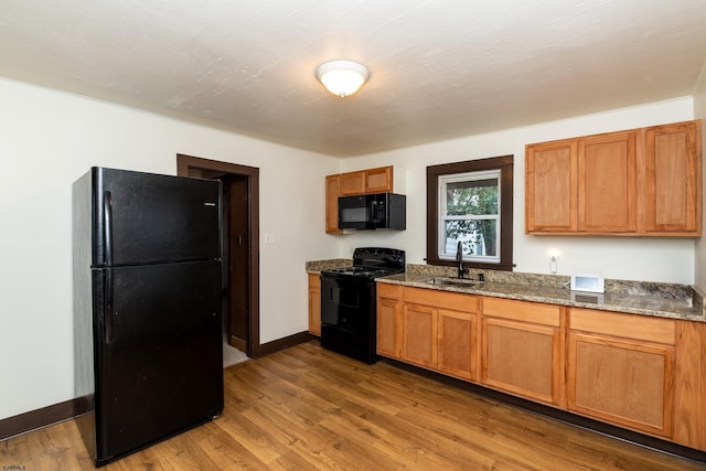 kitchen featuring a sink, stone counters, black appliances, and wood finished floors