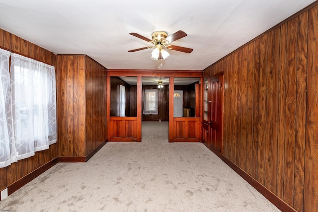 carpeted empty room featuring wood walls, ceiling fan, and a healthy amount of sunlight